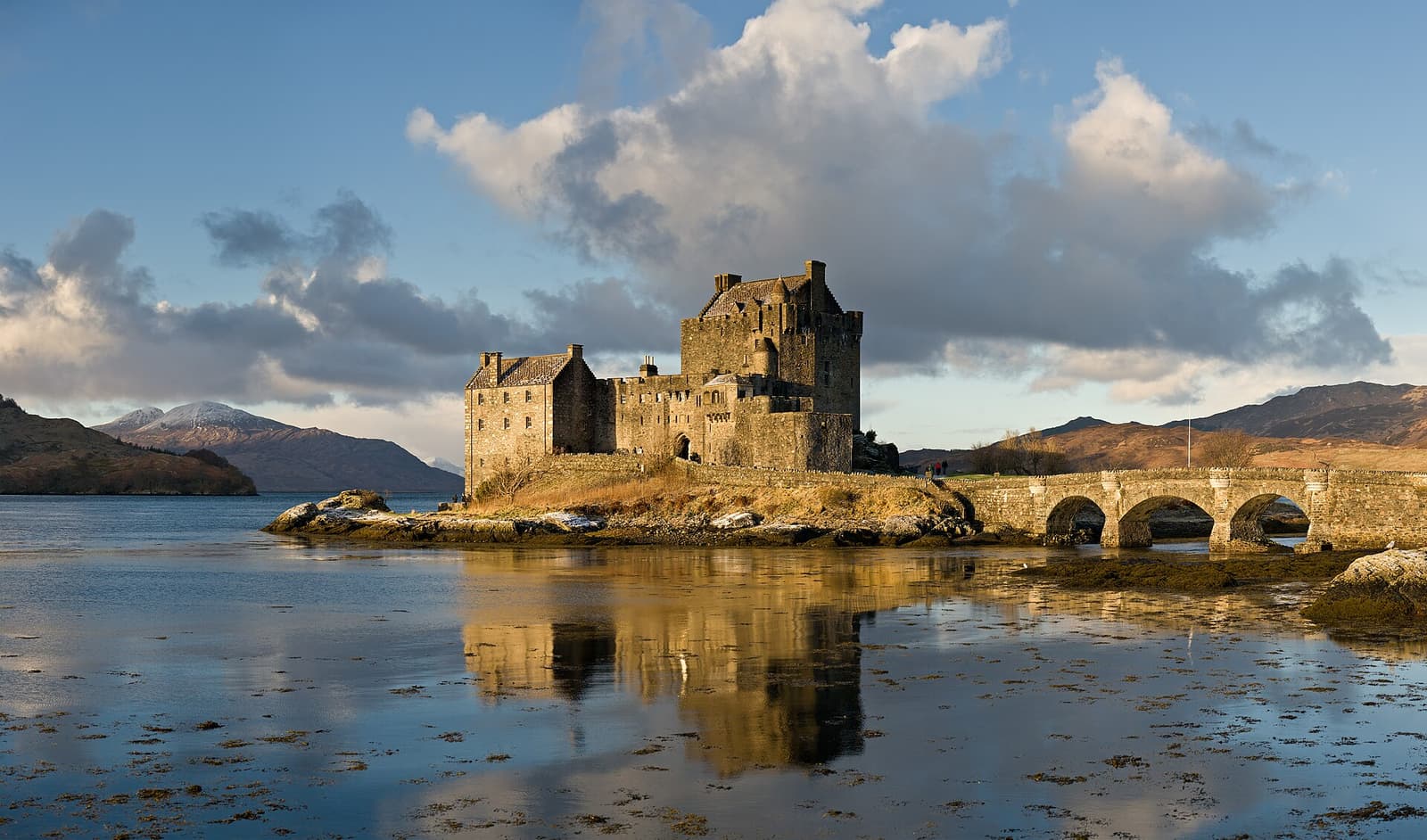Eilean Donan Castle on its small island, joined to the shore by a stone bridge, with mountains behind