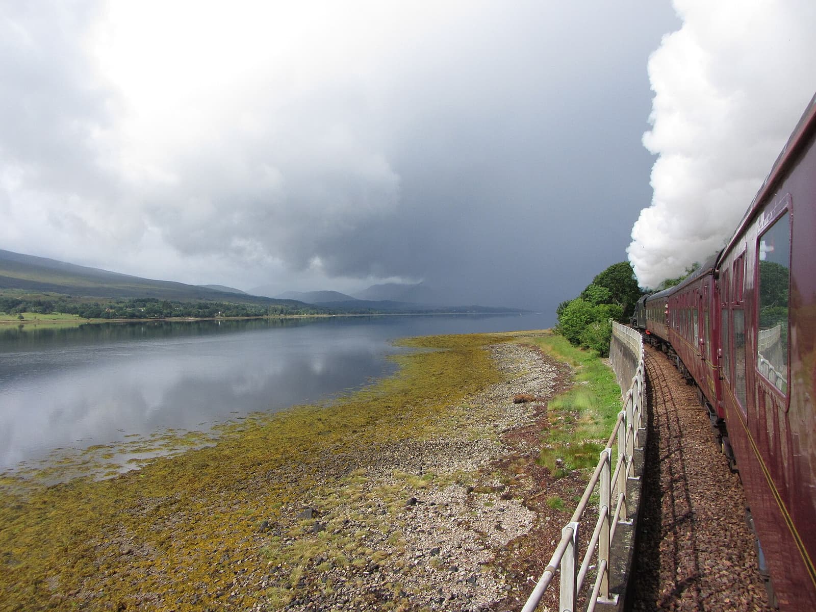 A steam train on the West Highland Line running along the shore of Loch Eil