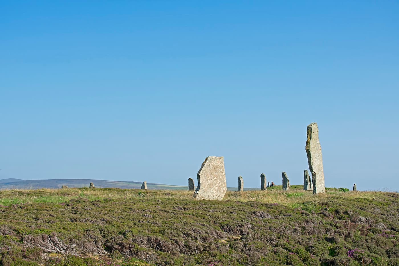 Standing stones of the Ring of Brodgar on heather moorland under a blue sky